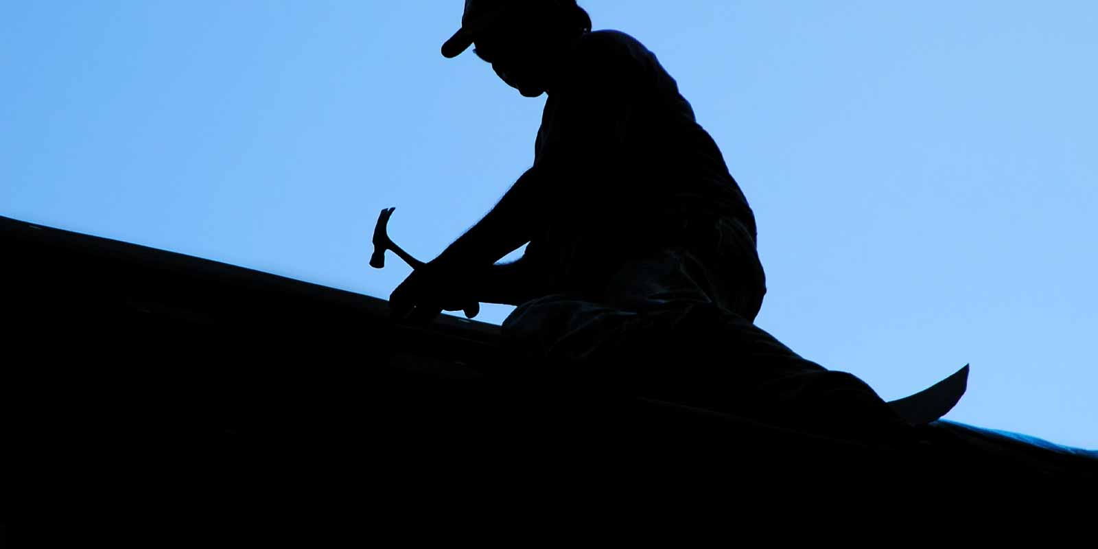 silhouette of man working on roof.
